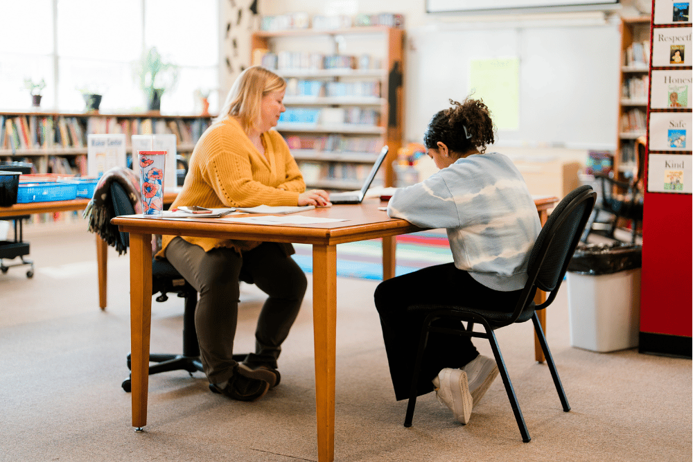 A teacher gives one on one tutoring with a student in the school library.