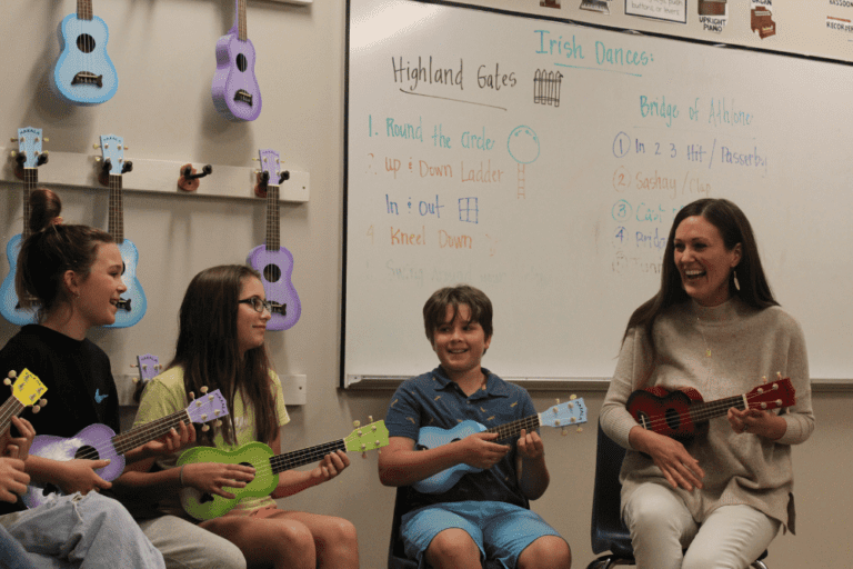 A music class sits in a circle holding ukuleles with the teacher.