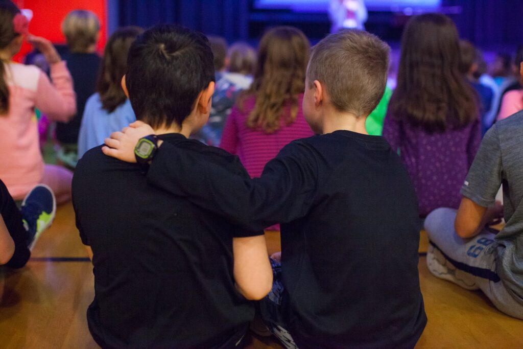 A boy puts his hand on friend's shoulder offering support during chapel meeting.