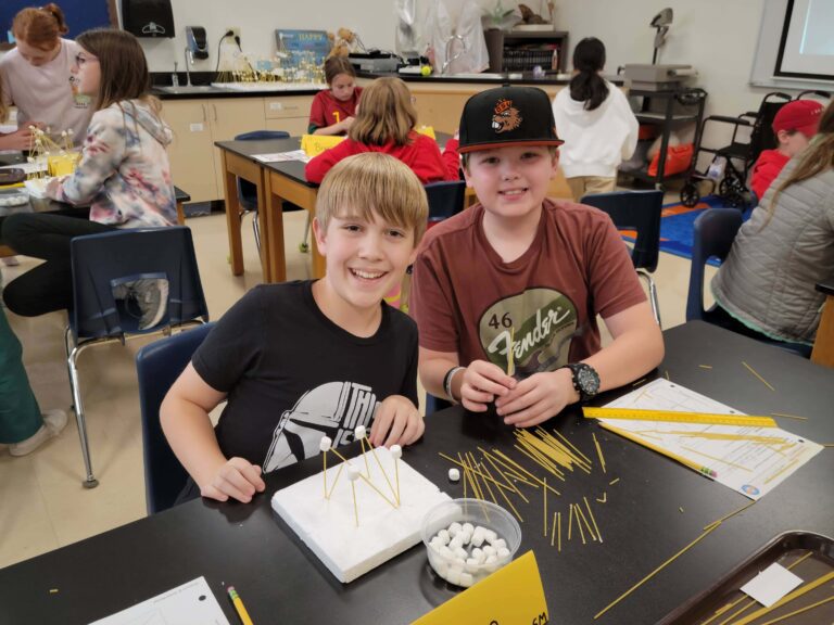 Two boys smile while working on engineering project in class.