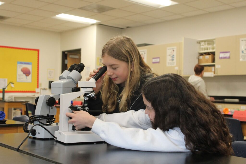 Two middle school girls use microscopes in science lab.