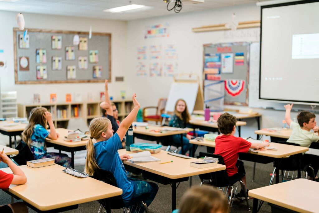 Several elementary students raise their hands in class.