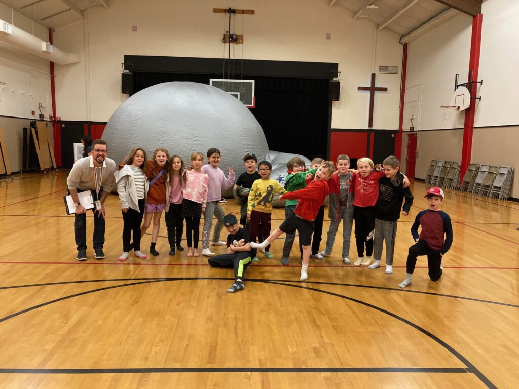 Elementary class takes a group photo with PE coach in gym.