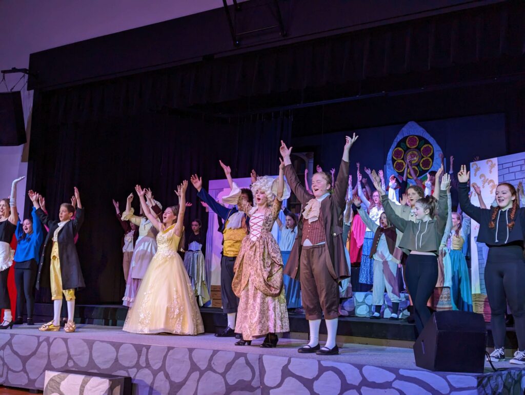 Large group of students in costumes take a bow from theater stage at West Hills Christian School.