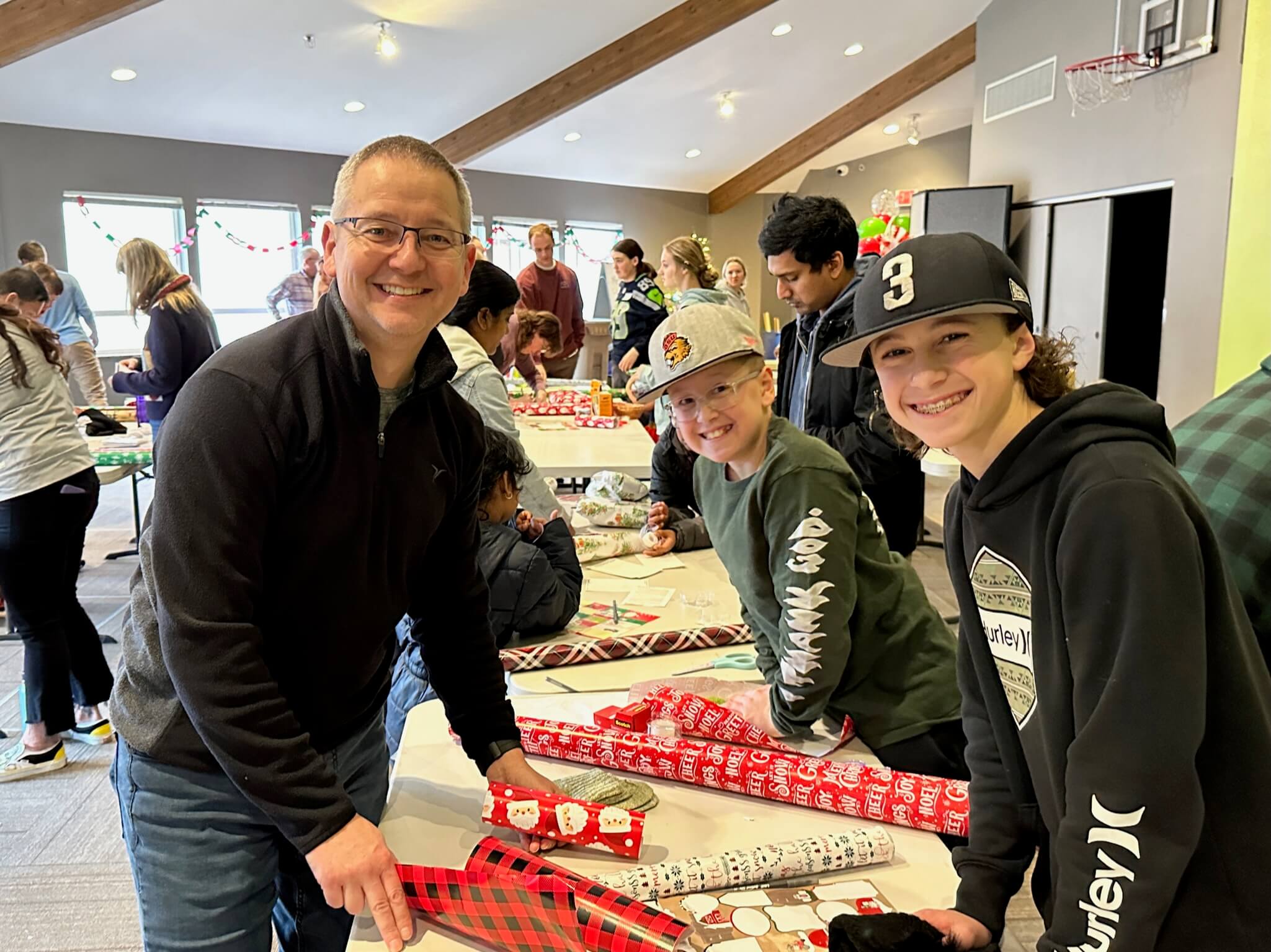 Two boys and a teacher wrap Christmas gifts at West Hills Christian School.