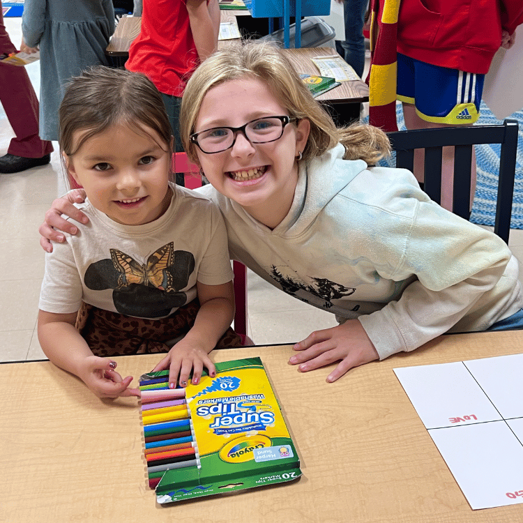Two Elementary girls smile for a photo as they draw with markers in class.