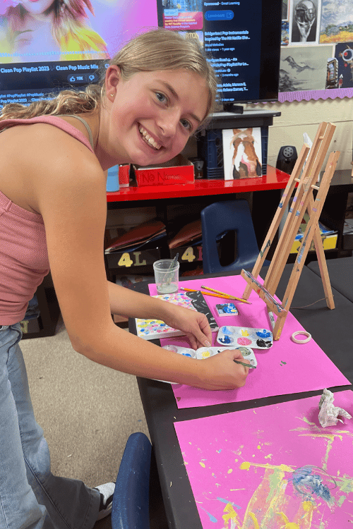 High School girl smiles while painting her artwork.