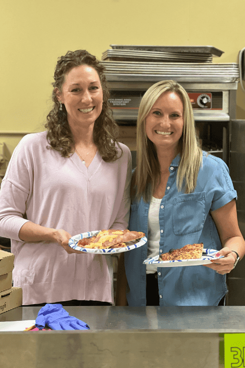 Two volunteers at West Hills Christian School help serve pizza to the students.