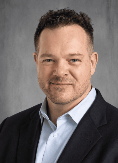 John Ewert, a professional with a friendly smile, wears a suit jacket and light blue shirt.